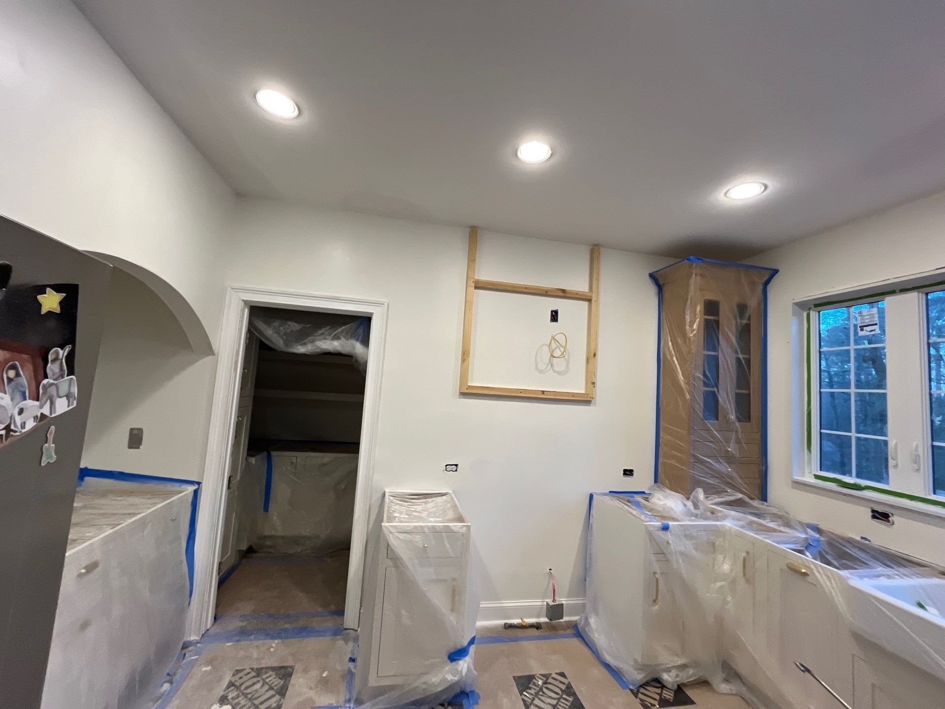 Kitchen renovation in progress โ new recessed lighting installed in ceiling, lower cabinets wrapped in plastic, upper cabinet framing โ Powder Springs, GA, Estate Solutions