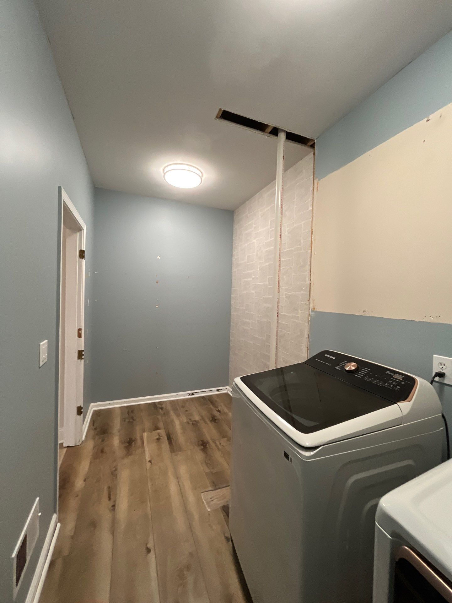 Laundry room after new flooring โ LVP hardwood installed, blue painted walls, washer and dryer in place, brick wall accent โ Powder Springs, GA, Estate Solutions